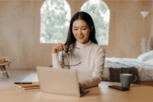 Mulher asiática sorrindo enquanto navega no notebook, simbolizando o momento de investir em um site profissional para impulsionar sua presença digital